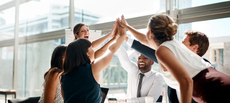 Shot of a group of businesspeople high fiving while sitting in a meeting